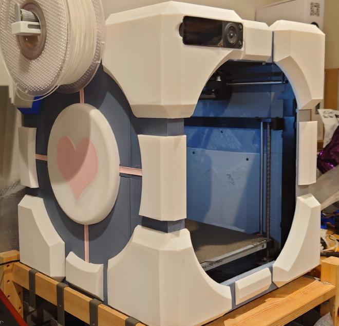 A bambulab P1P 3D printer with grey and white custom panels which make it look like a companion cube from the game Portal